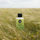Tallow-Licious Honey Milk Whipped Moisture Cream bottle in a field of grass surrounded by wildflowers.